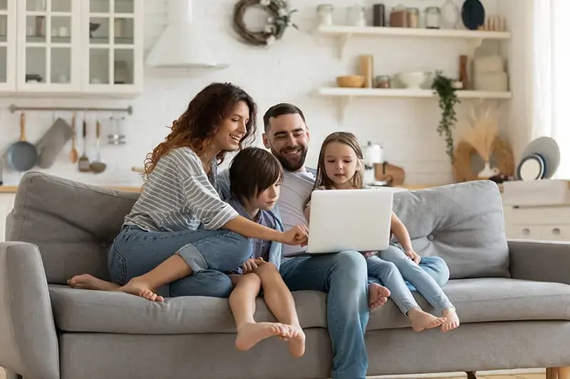 Happy-young-family-with-little-kids-sit-on-sofa-in-kitchen-have-fun-using-modern-laptop-together