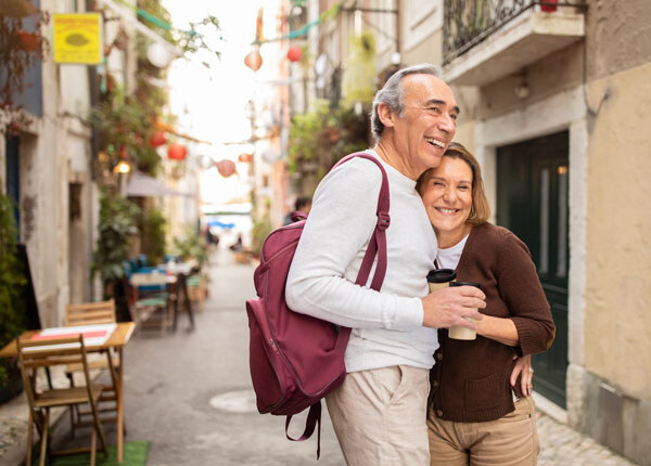 joyful-senior-tourists-couple-hugging-posing-with-backpack-holding-paper